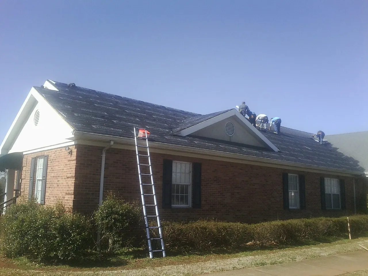 Crew tearing shingles off a brick ranch roof with a ladder set — Metal Roof Repair work by our crew in Atglen