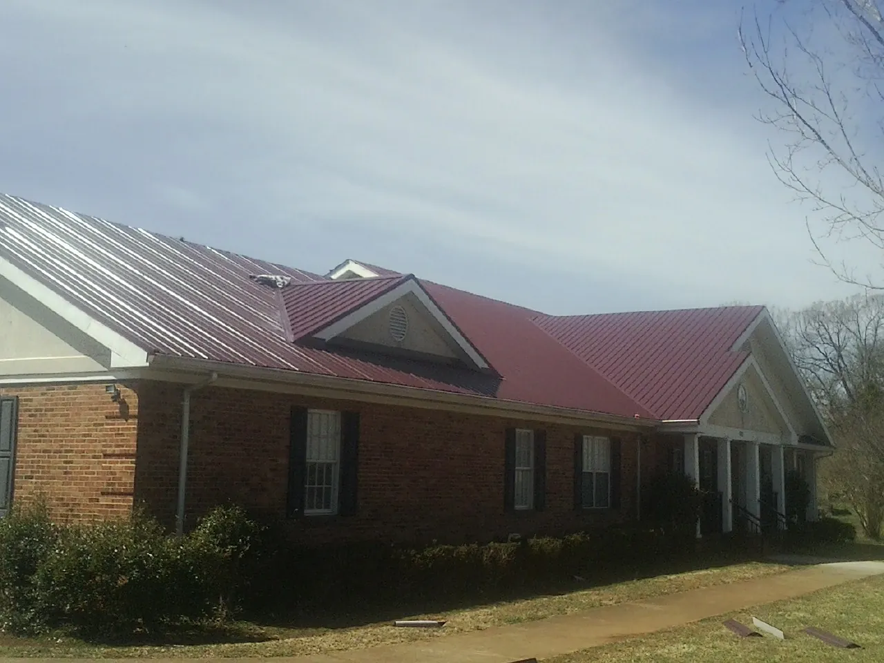 Red metal roof with gabled entries on a long brick building, from a Hail Damage Roof Repair job in Atglen