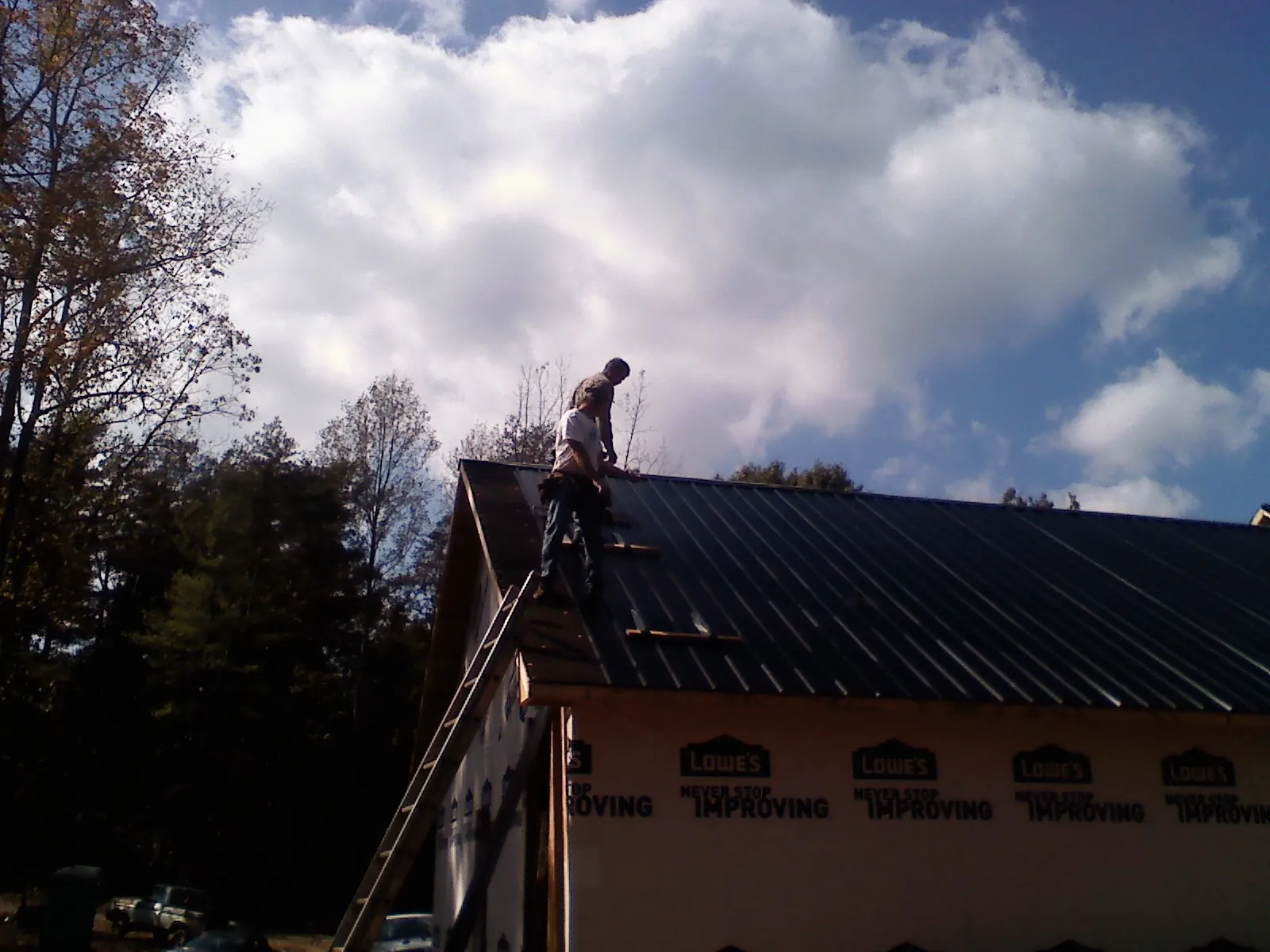 Roofer fastening dark metal panels high against a cloudy sky, from a Roof Inspection job in Atglen