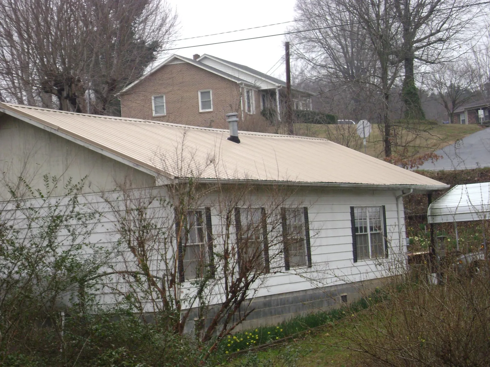 Tan metal roof on a white sided house set into a hillside — Commercial Roofing by Roofing Brothers in Atglen